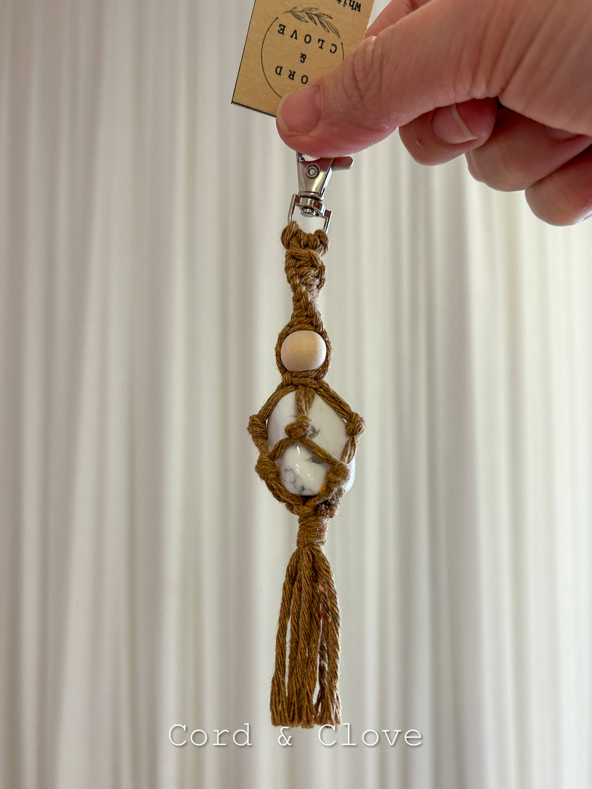 Handmade crystal macramé keychain held by a hand against a neutral background