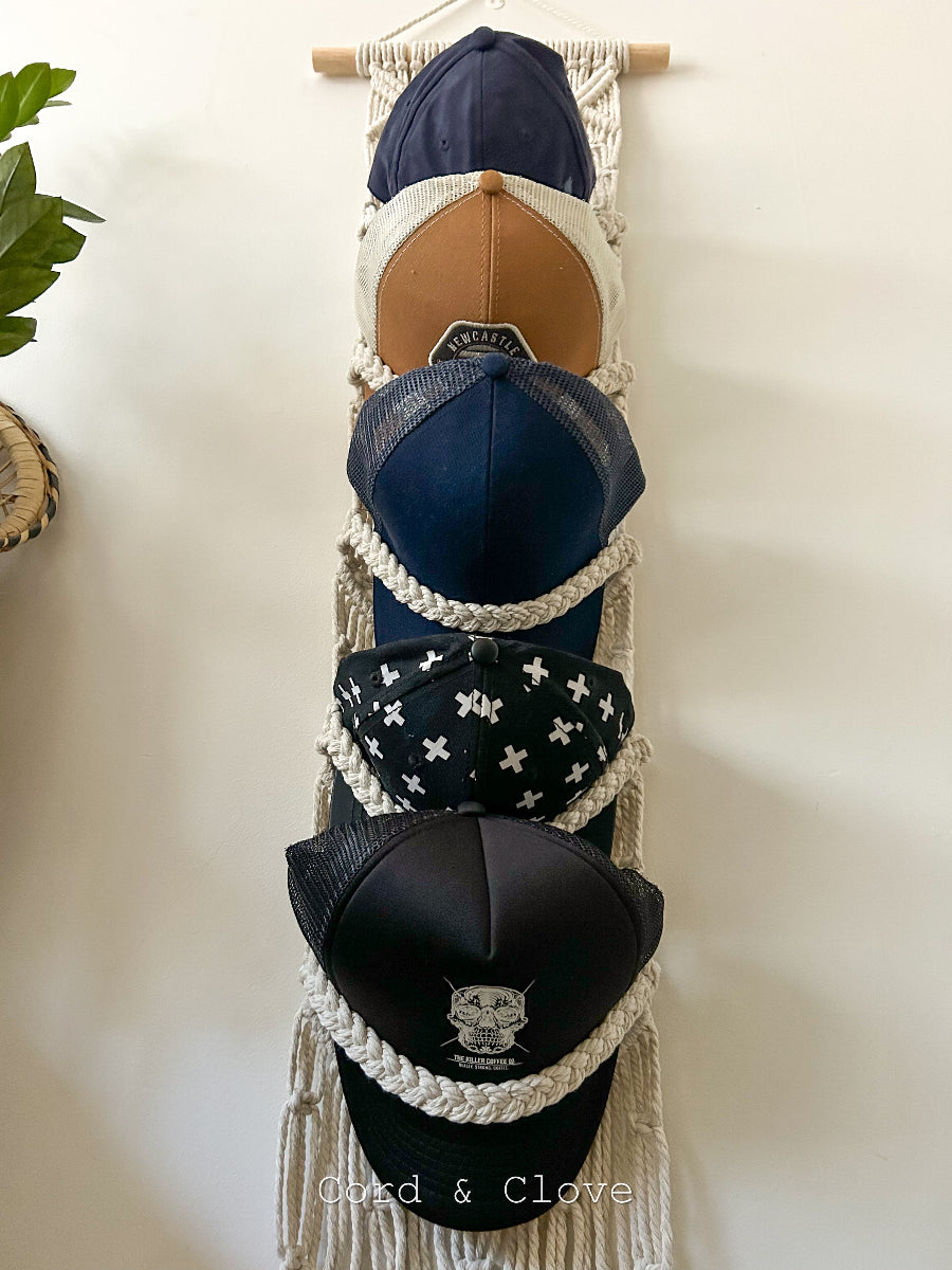 Collection of baseball caps displayed on a macramé wall hanger against a white background.