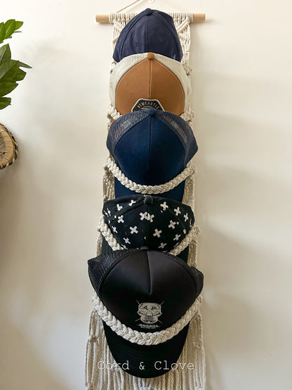 Collection of baseball caps displayed on a macramé wall hanger against a white background.
