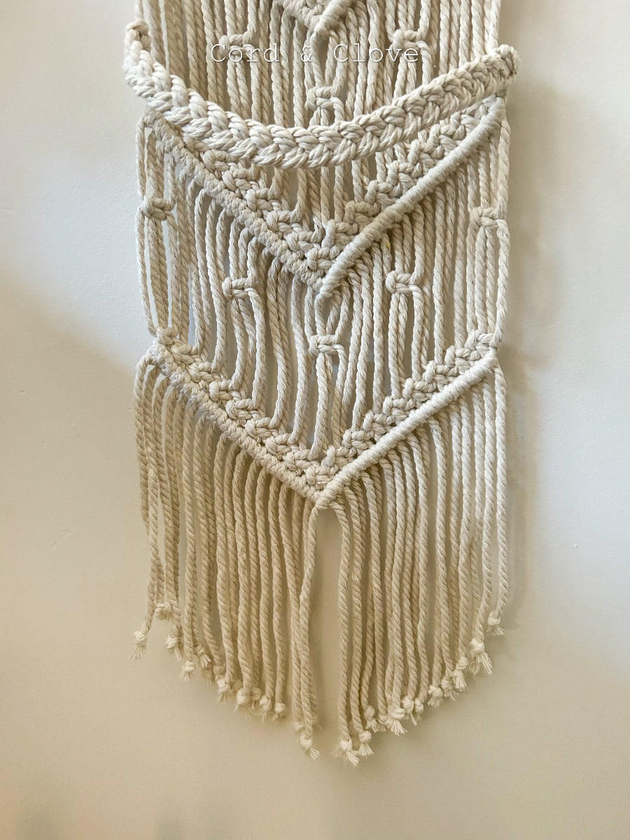 Macrame wall hanging with fringes on a plain background
