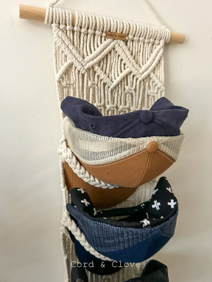Macrame wall hanging with cap storage slots on a plain background
