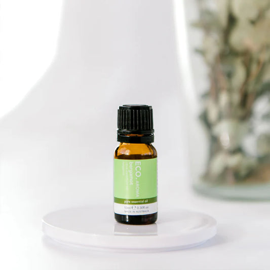 A 10ml bottle of Eco Modern Essentials pure bergamot essential oil with a green label on a white surface, with a blurred background suggesting a soft-focus effect.