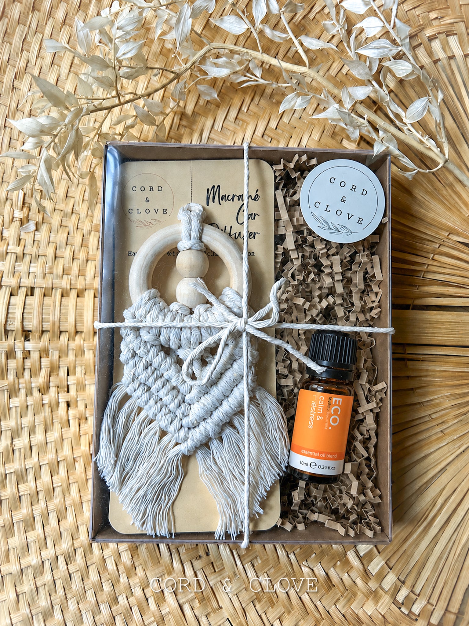 Gift set with macrame car diffuser and essential oil bottle on a woven surface