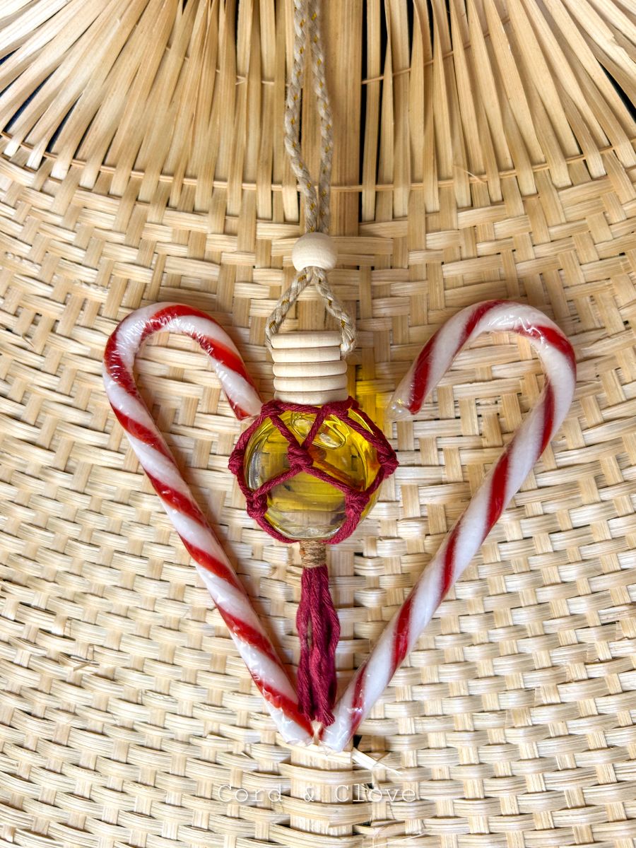 Hanging car diffuser bottle filled with essential oils,  styled beside candy cane sticks on a woven surface