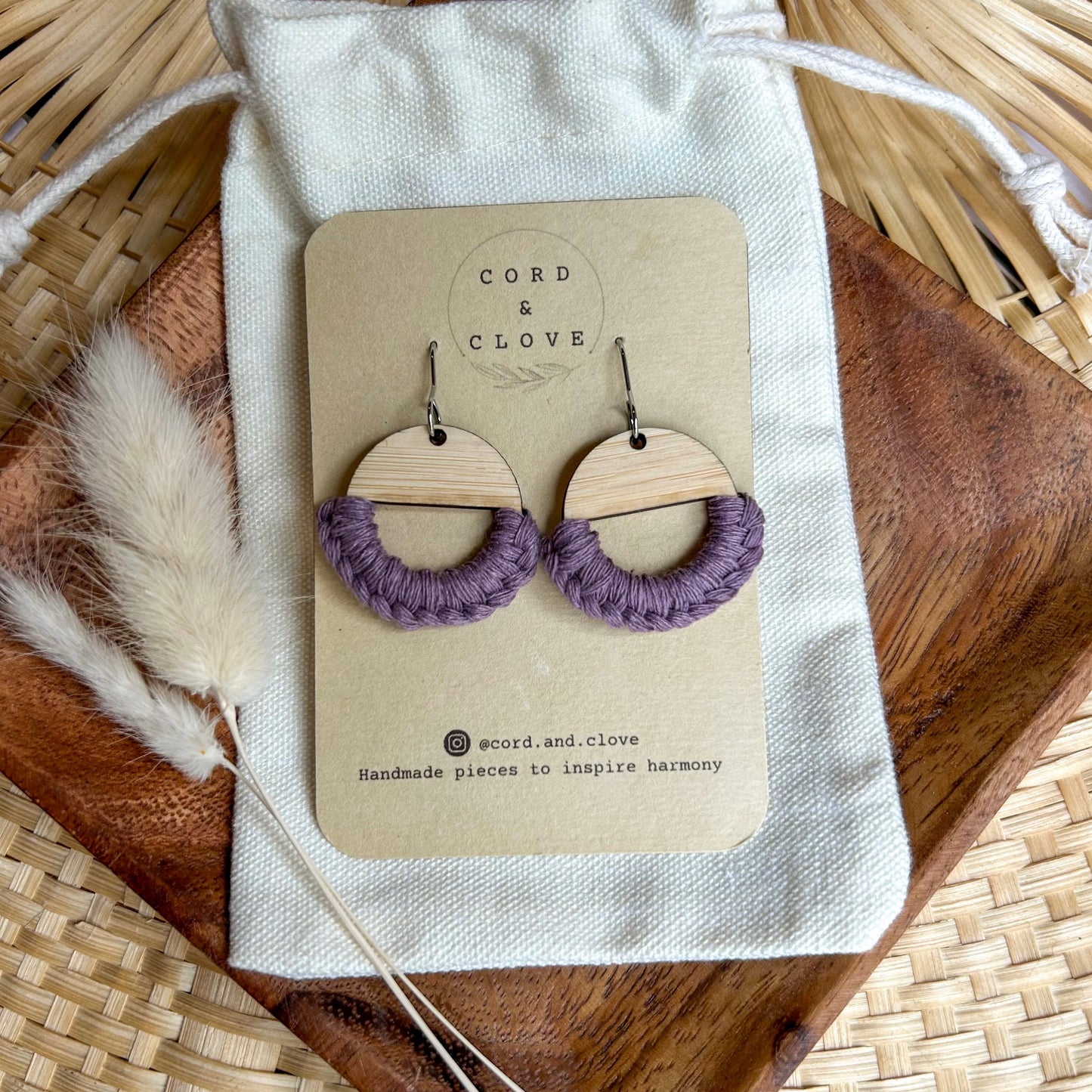 Pair of wooden earrings with purple loops on a 'Cord & Clove' branded card, placed on a woven surface.