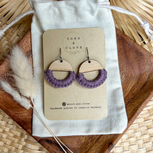 Pair of wooden earrings with purple loops on a 'Cord & Clove' branded card, placed on a woven surface.