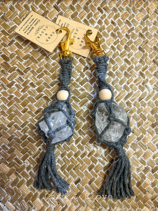 Pair of gray macrame crystal keyrings with gold clasps on a textured brown background