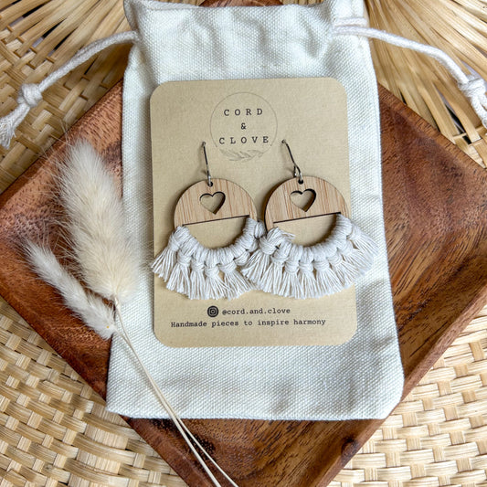 Wooden heart-shaped earrings with macrame details on a 'Cord & Clove' branded card, placed on a woven surface.