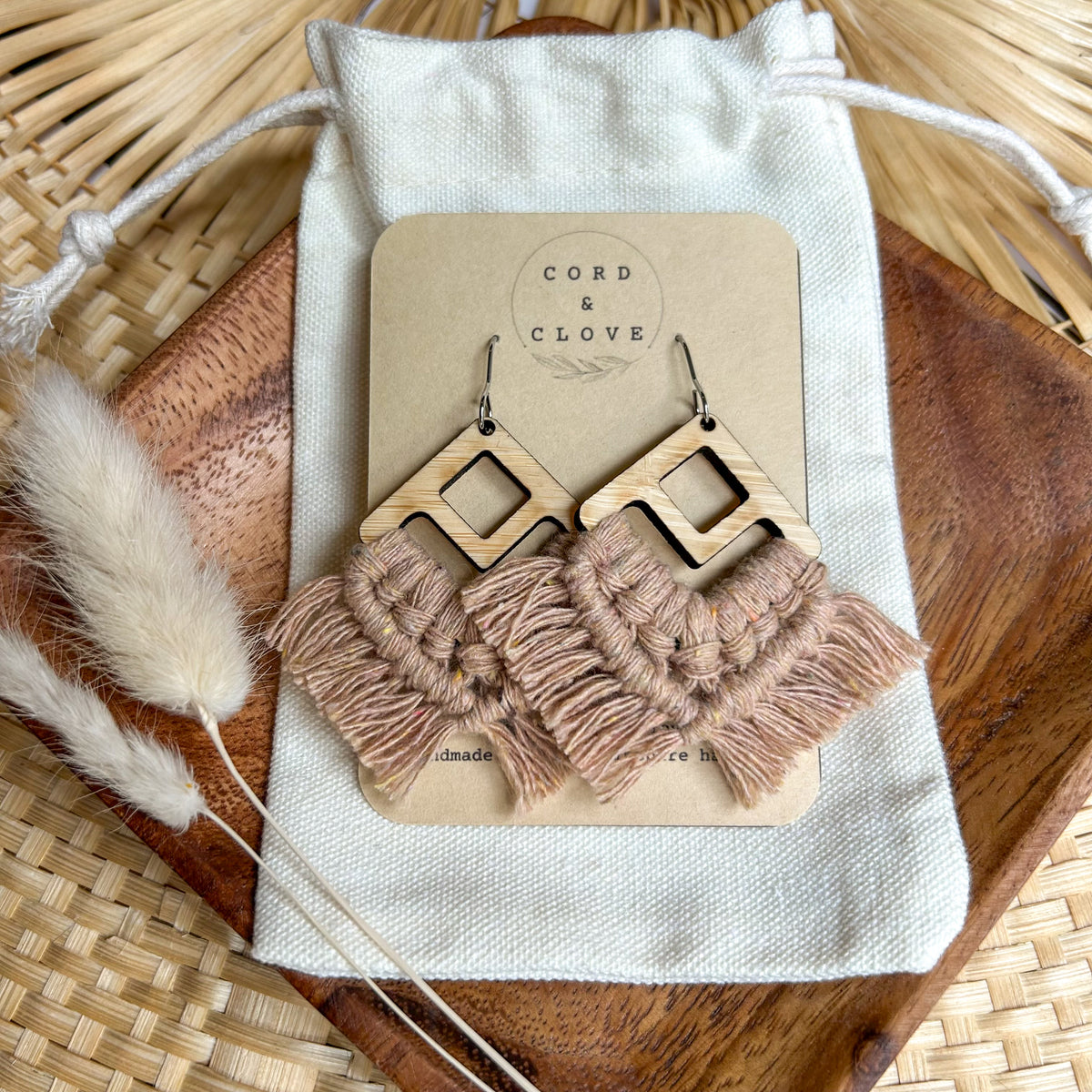 Pair of earrings with tassel details on a 'Cord & Clove' branded card, placed on a textured surface.