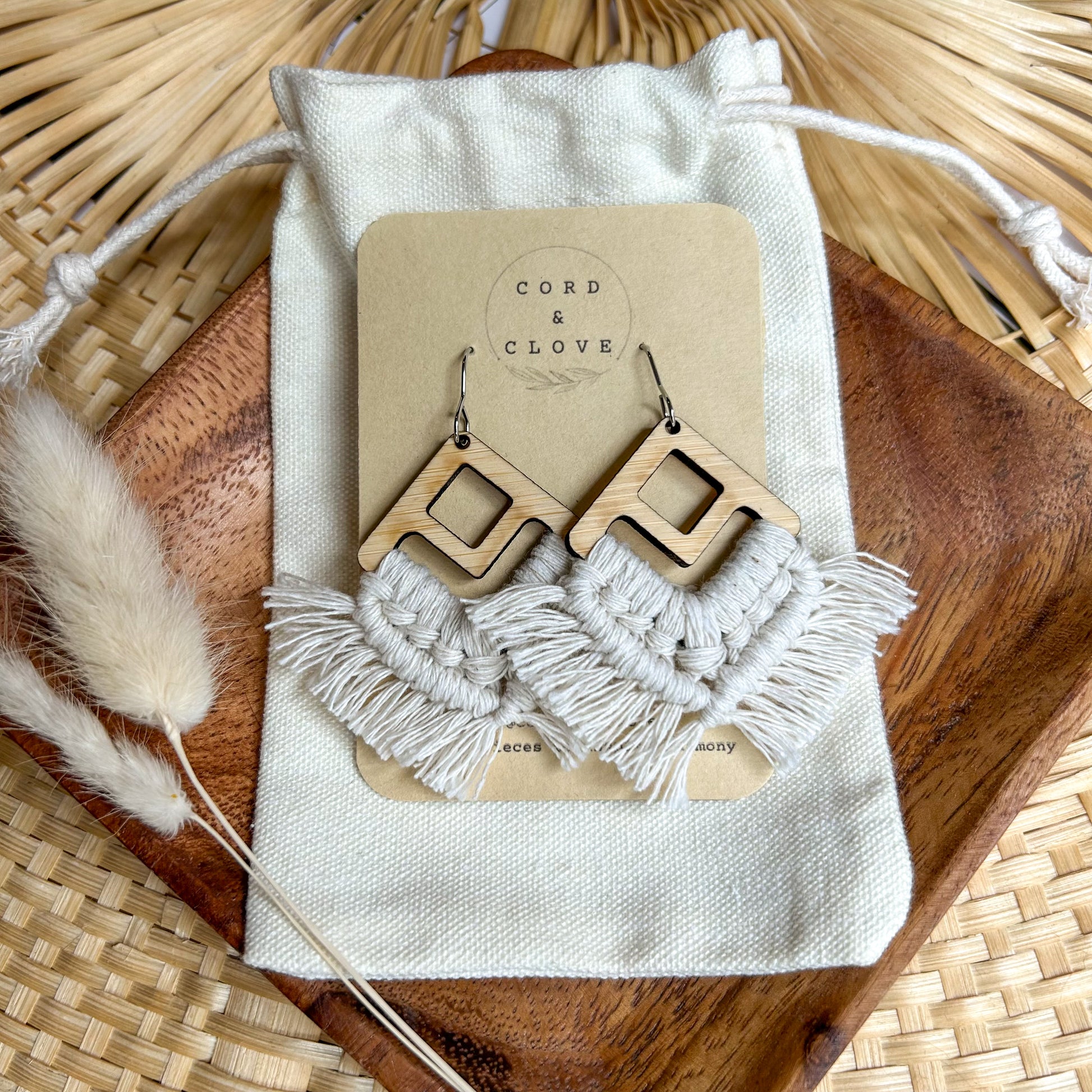 Macrame earrings with wooden accents on a 'Cord & Clove' branded card, displayed on a textured surface.