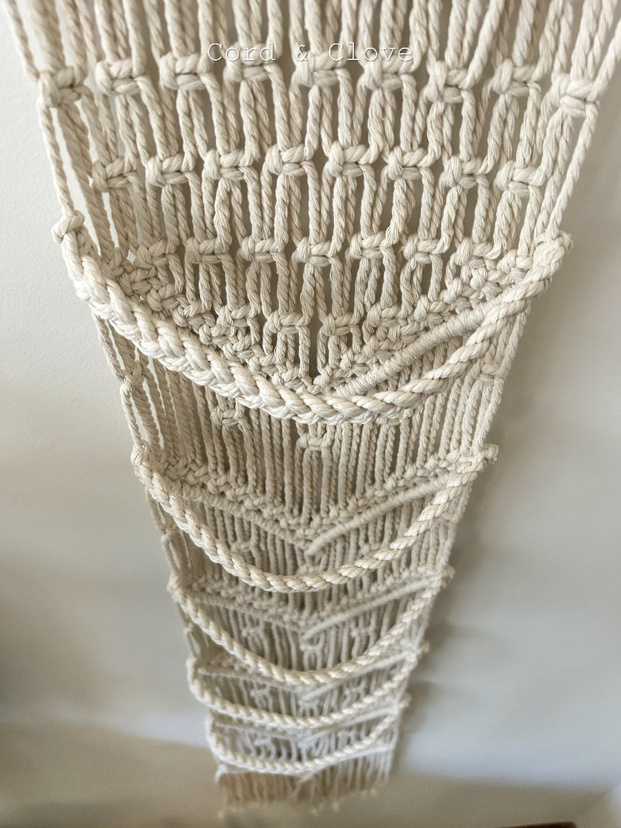 Close-up of a textured beige macrame wall art piece on a white background
