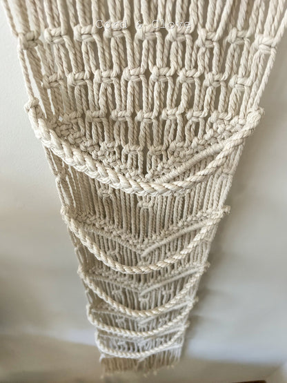 Close-up of a textured beige macrame wall art piece on a white background