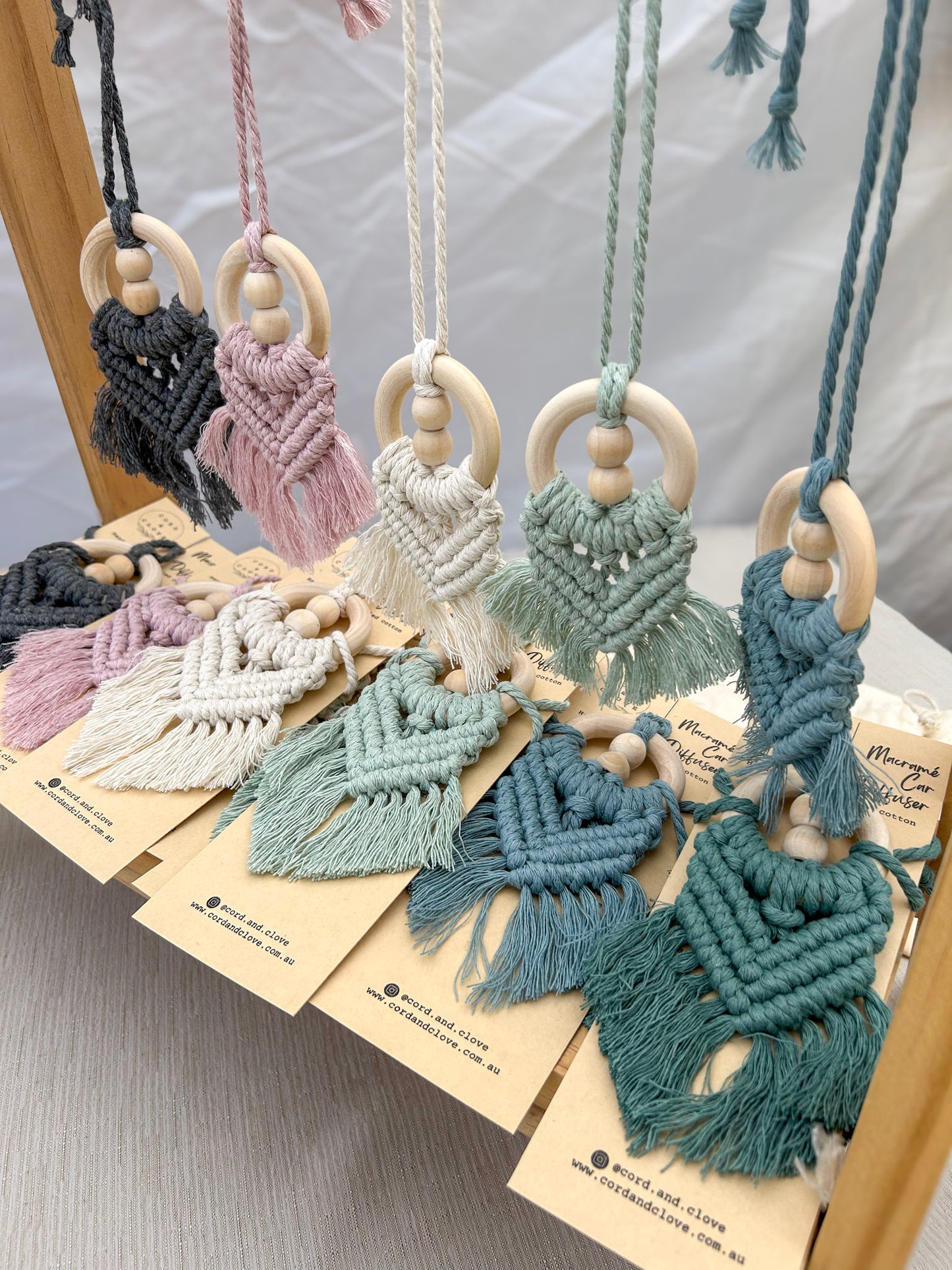 Hanging macrame essential oil car diffusers in various colours with wooden beads on a white surface