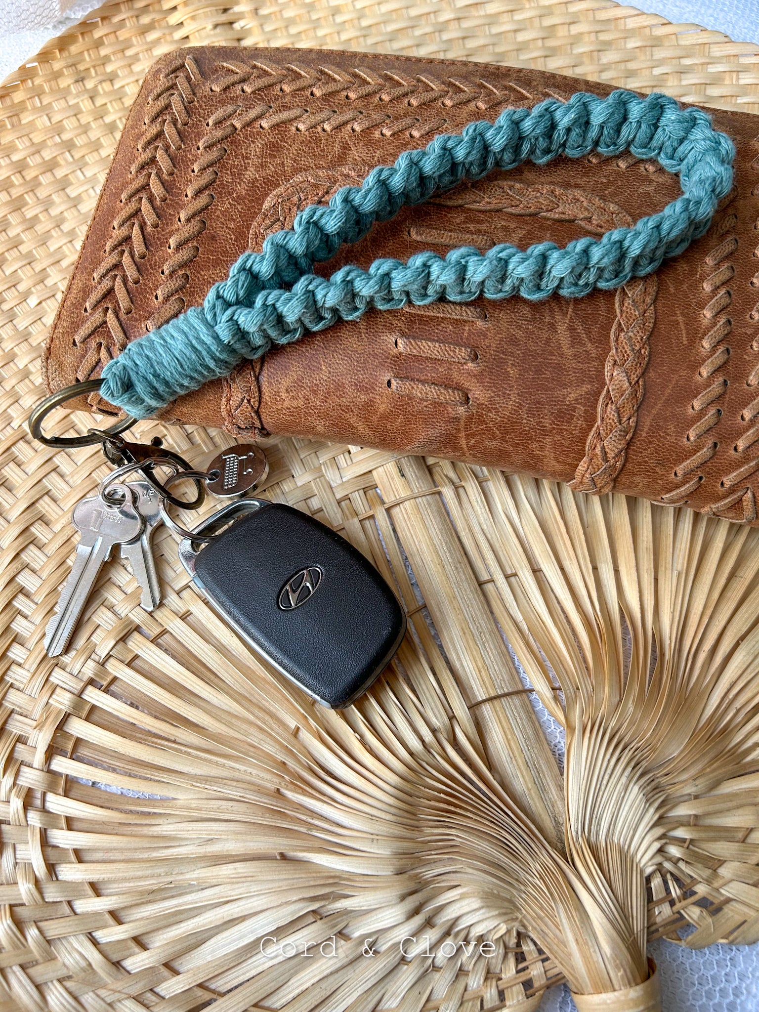 Teal keychain with keys attached to a brown leather wallet on a woven surface