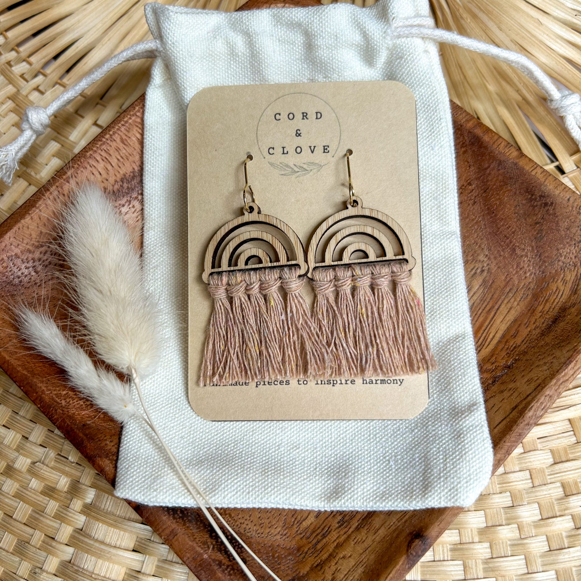 Wooden rainbow earrings with tassels on a 'Cord & Clove' branded card, placed on a woven surface.